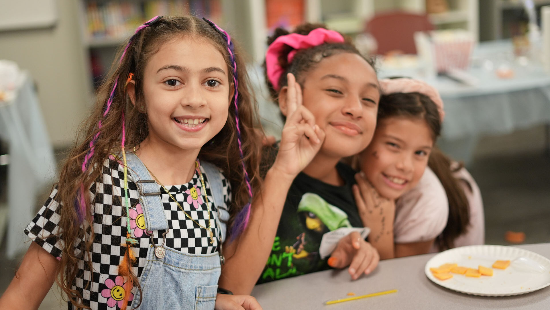 3 girls at a table, smiling and embracing each other with a small snack plate.