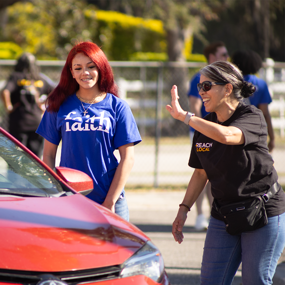 lady wearing black t-shirt waving to driver in red car