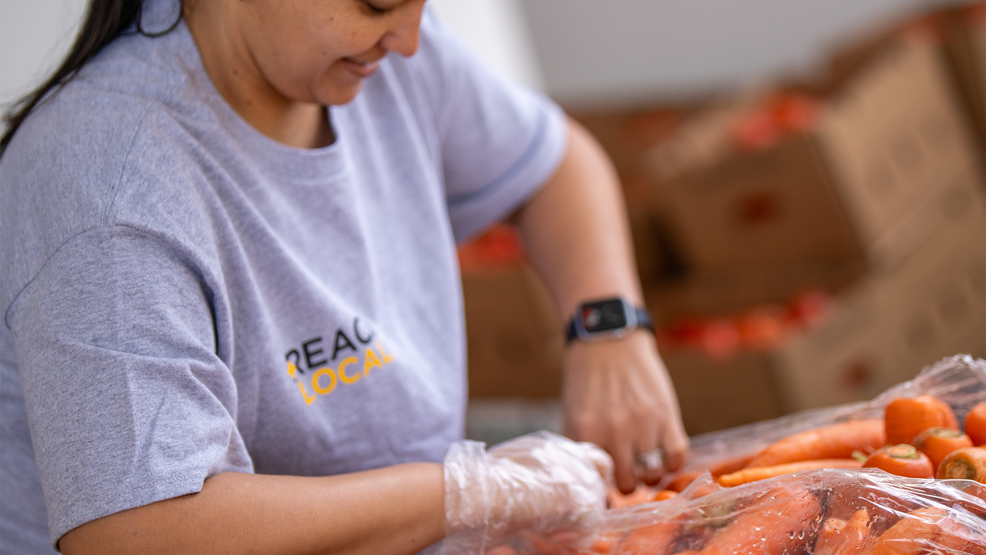 woman smiling wearing gloves reaching into a bag of carrots.